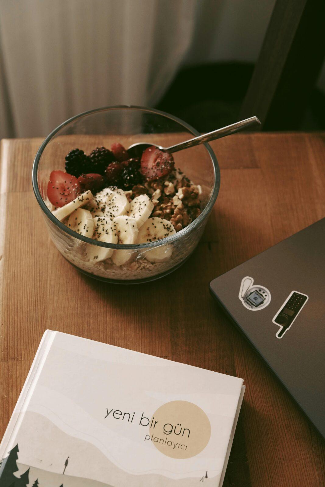 A delicious bowl of granola with fruit toppings beside a planner and laptop.